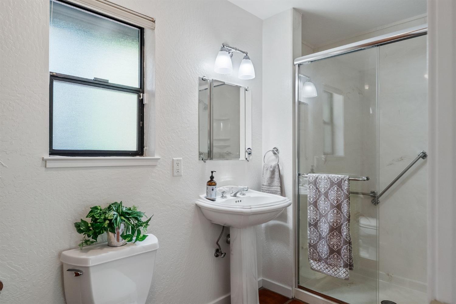 Primary bathroom #2 features a pedestal sink, custom lighting/medicine cabinet mirrors, upgraded shower glass doors and built-in cabinets.