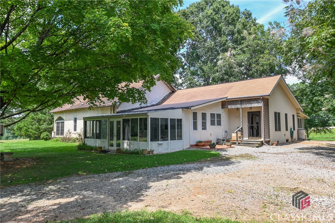 The Seller is offering a Temporary 2-1 Buydown, reach out to the listing agent for details. Lovingly maintained 1915 home in a peaceful setting overlooking mature hardwoods and pastureland in the heart of Oconee County on 2.82 acres! This home has been in the same family for generations and still has some of the original oak and heart pine wood floors and three original mantels. There are multiple porches around the home to enjoy the view of flowers and mature landscaping. There is a four seasons sunroom with a sink, a screened porch next to the kitchen and keeping room, and an enclosed front porch off the primary bedroom. The kitchen has many convenient features including an island with a sink, an appliance garage, a mixer lift, glass-fronted upper cabinets, a Lazy Susan corner cabinet, and a downdraft gas cooktop. There is a large office space with a built-in desk and wall cabinets. Energy-efficient HVAC was installed in 2021. The primary bedroom has the original floors and fireplace. A second bedroom is located off the main hallway, across from the large office.  A metal outbuilding/workshop is ready for your projects! The property is connected to public water. With a few updates, there is so much potential!