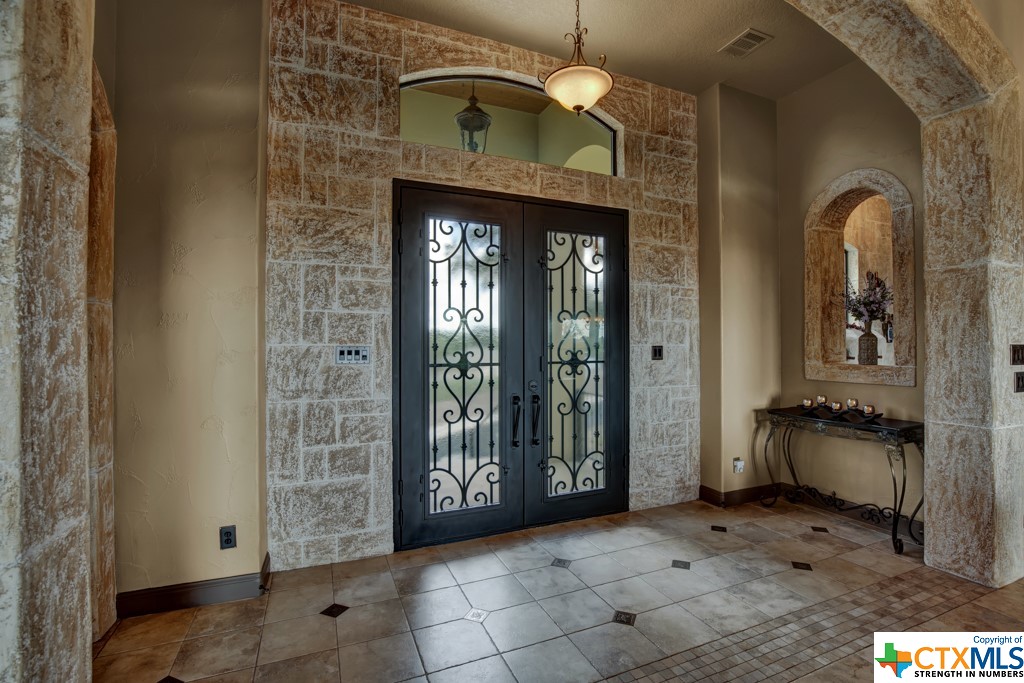 Entry features double metal & glass decorative doors, coolstone accents, and tile flooring