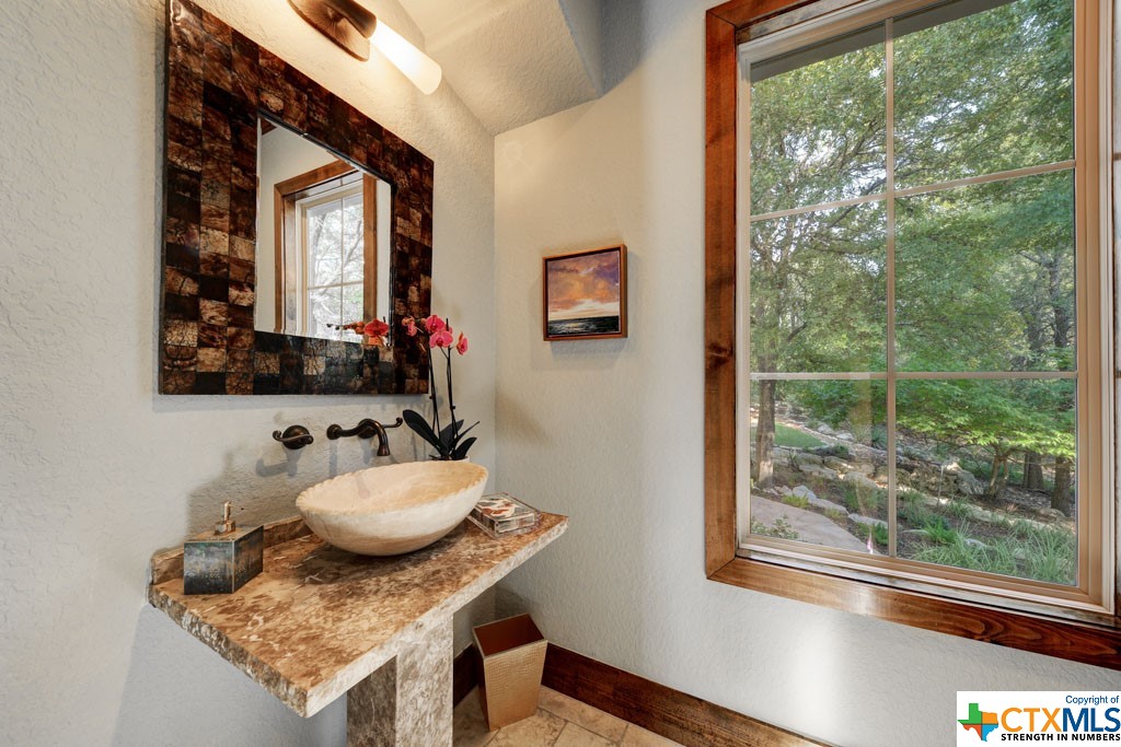 This captivating view of a pristinely landscaped yard accompanies a unique counter, sink and wall mounted faucet in the singular half bath.