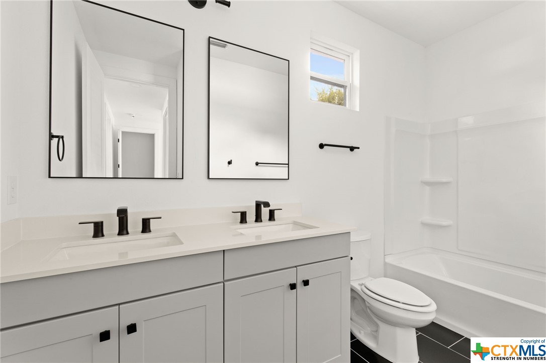 Secondary bathroom with shower/tub, double vanity, and quartz countertop.
