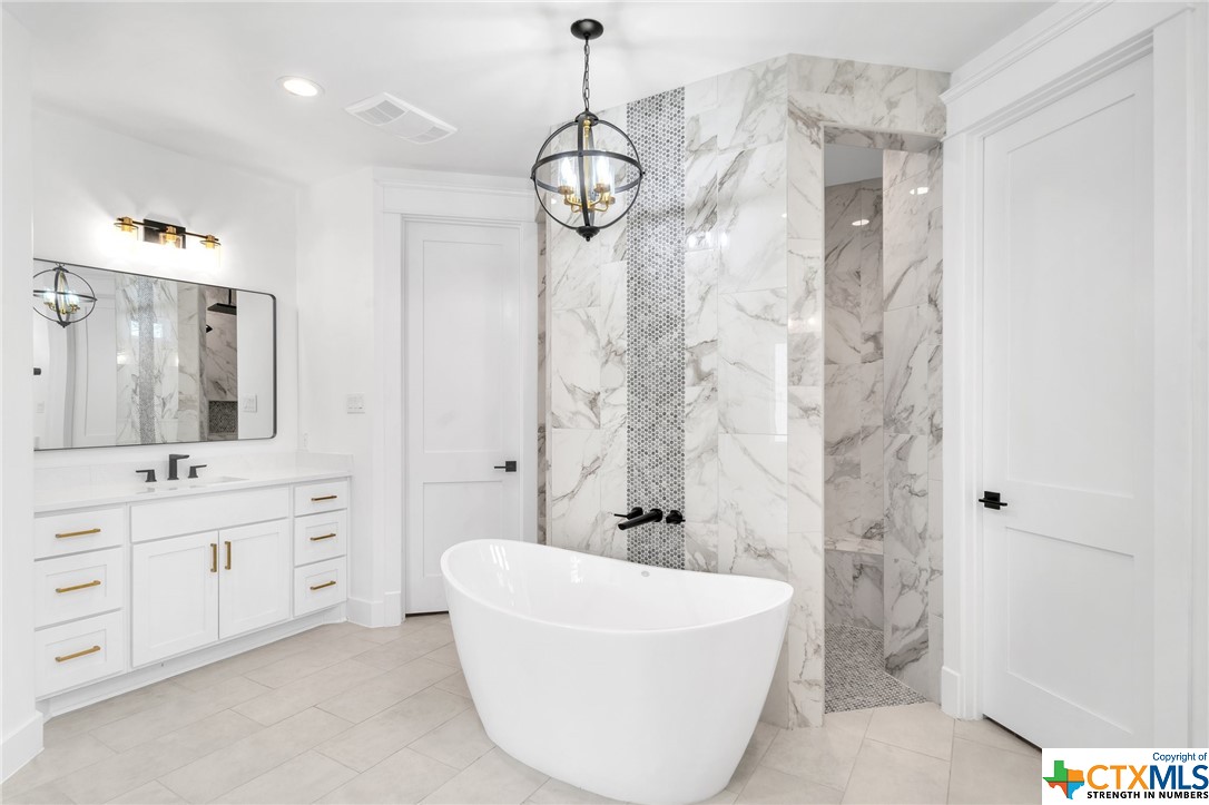 Marbled tile in walk through shower, soaking tub, separate vanities, sleek plumbing fixtures and marbled quartz counters
