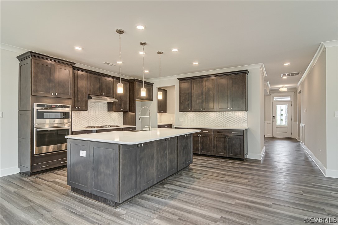 Photo represents the plan, not the actual home. Design selections may vary. DESIGNER kitchen features gray cabinetry, granite counters, tile backsplash, gas cooktop, and built-in wall oven is open to the family room.