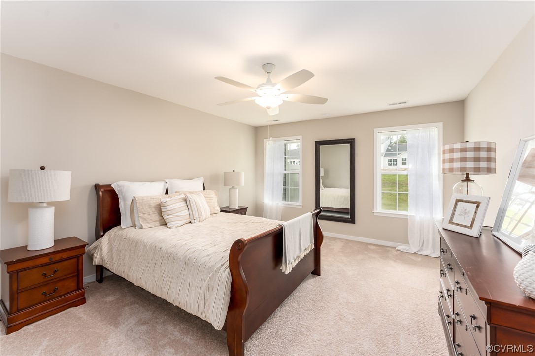 Bedroom featuring light carpet, multiple windows, and ceiling fan