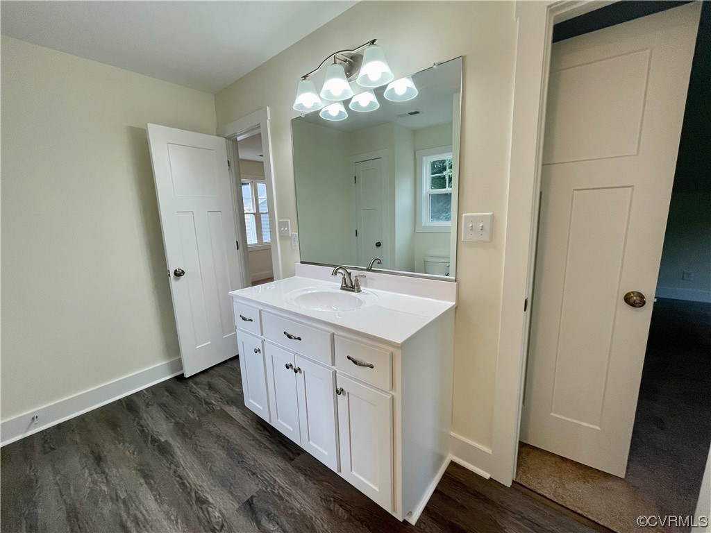 shared bathroom featuring wood-type flooring, toilet, mirror, and vanity