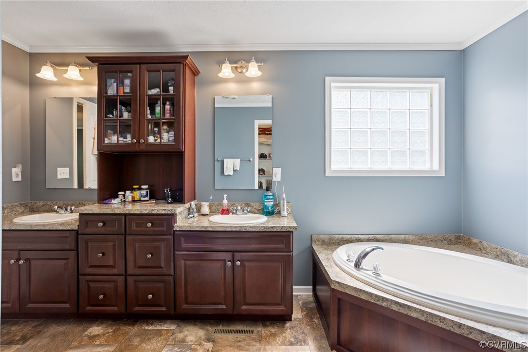 Bathroom featuring dark tile floors, a bath, mirror, dual vanity, and ornamental molding