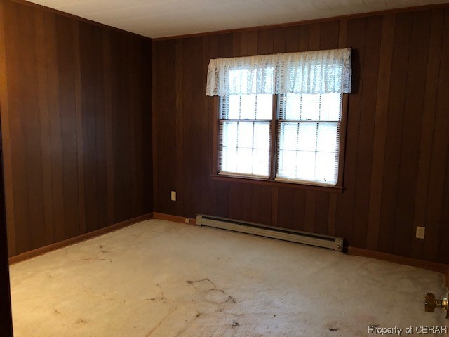 Carpeted empty room with wooden walls, plenty of natural light, and a baseboard heating unit