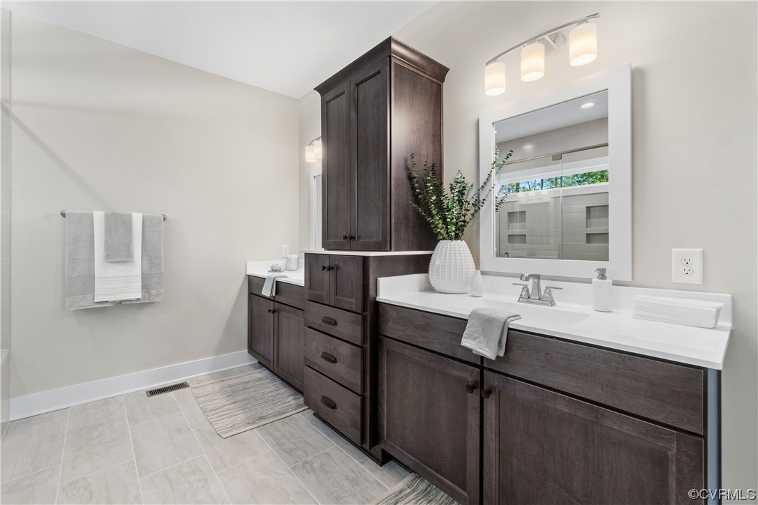 Bathroom featuring double sink, tile floors, and vanity with extensive cabinet space