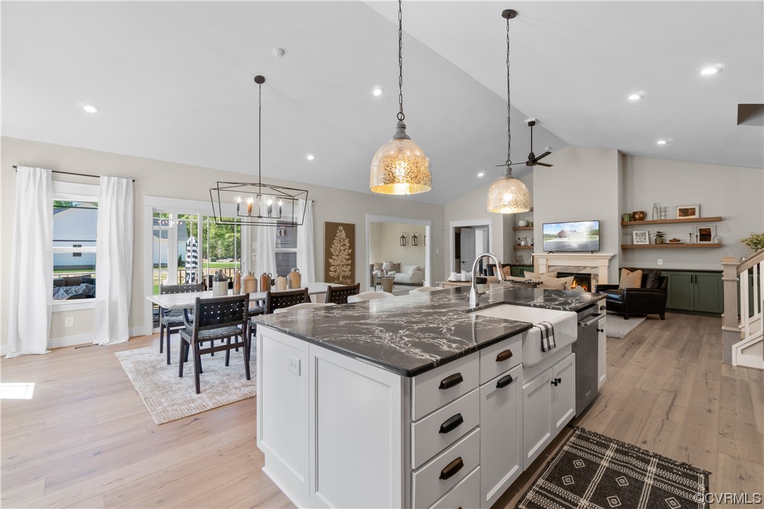 Kitchen featuring light hardwood / wood-style floors, white cabinets, an island with sink, a notable chandelier, and pendant lighting