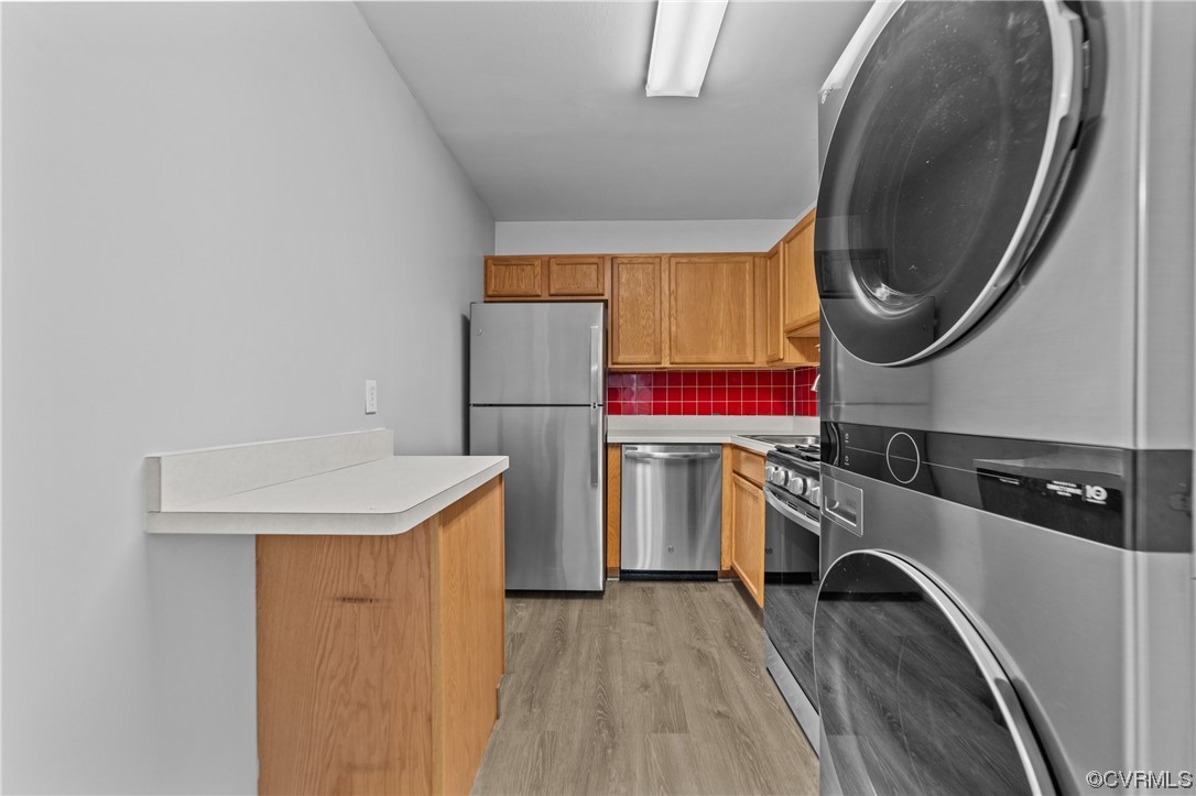 Laundry room featuring stacked washer / dryer and light hardwood / wood-style flooring