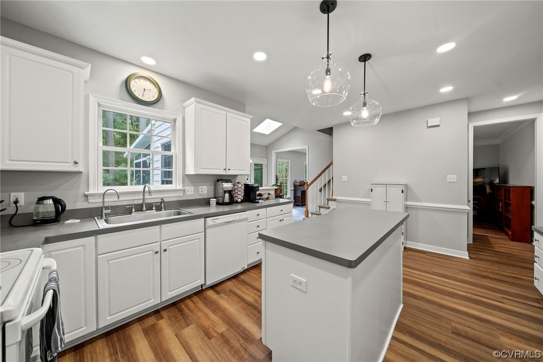 Kitchen with white cabinetry, range, hardwood floors, white dishwasher, washer and clothes dryer, and hanging light fixtures