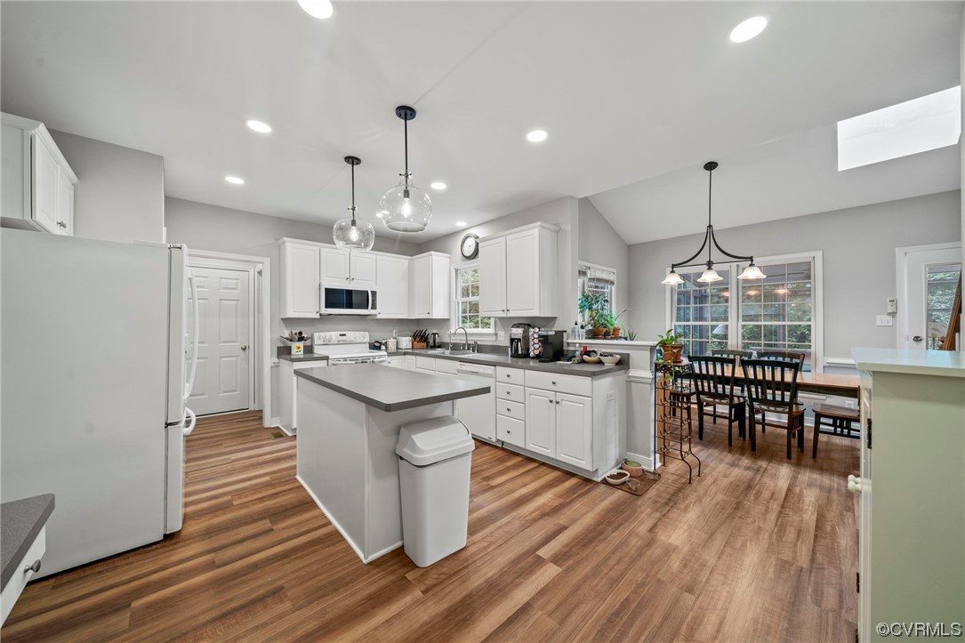 Kitchen featuring pendant lighting, an island with sink, white cabinets, lofted ceiling, a wealth of natural light, light countertops, white appliances, and light hardwood floors