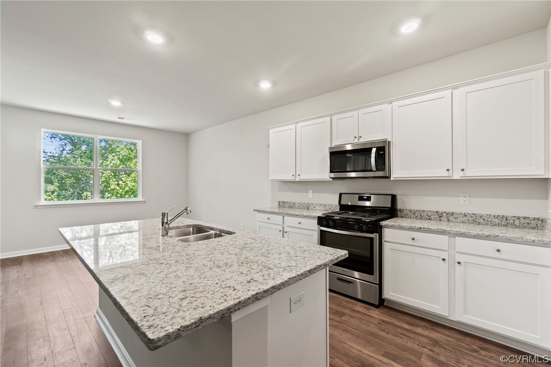 Kitchen featuring sink, white cabinets, a center island with sink, dark hardwood floors, and stainless steel appliances