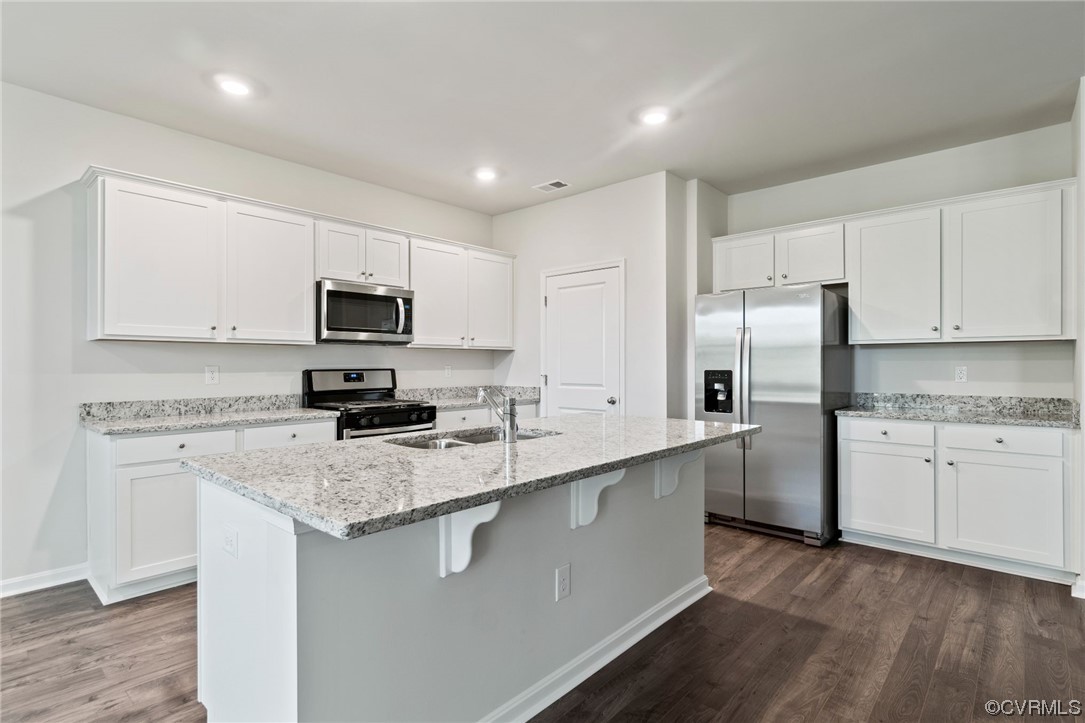Kitchen with stainless steel appliances, dark hardwood flooring, white cabinets, and a kitchen island with sink
