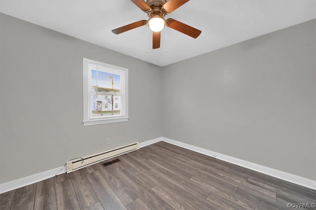 Empty room featuring a baseboard heating unit, dark hardwood floors, and ceiling fan