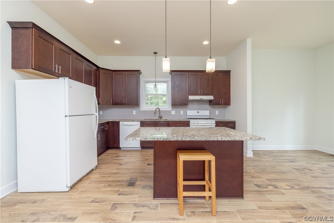 Kitchen featuring a center island, granite counters, hanging light fixtures, backsplash, and white appliances