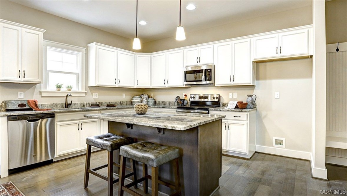 Kitchen with hanging light fixtures, appliances with stainless steel finishes, light hardwood / wood-style floors, white cabinets, and tasteful backsplash