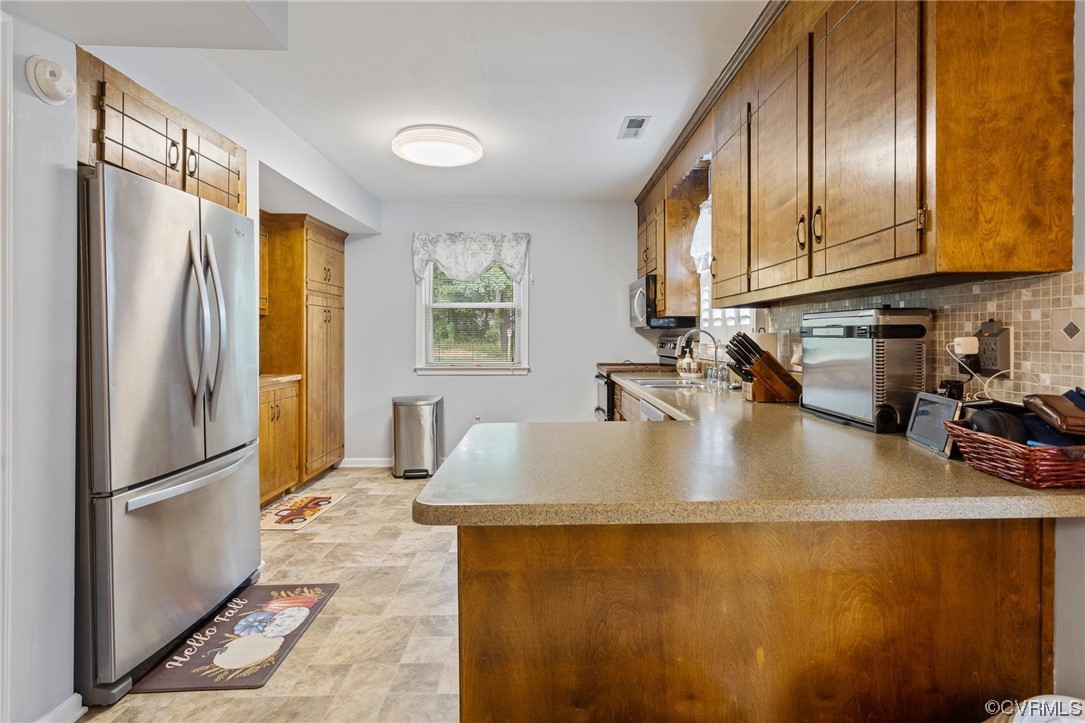Kitchen featuring sink, light tile floors, backsplash, appliances with stainless steel finishes, and kitchen peninsula