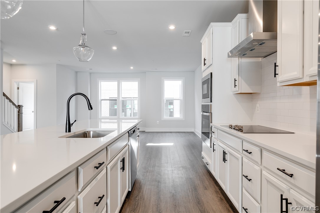 Kitchen featuring white cabinetry, dark hardwood flooring, wall chimney exhaust hood, and pendant lighting