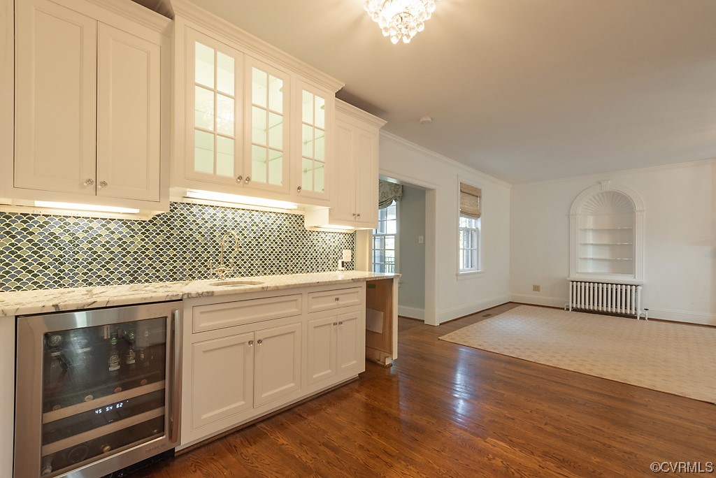 Kitchen with radiator heating unit, dark hardwood flooring, wine cooler, white cabinets, and a chandelier