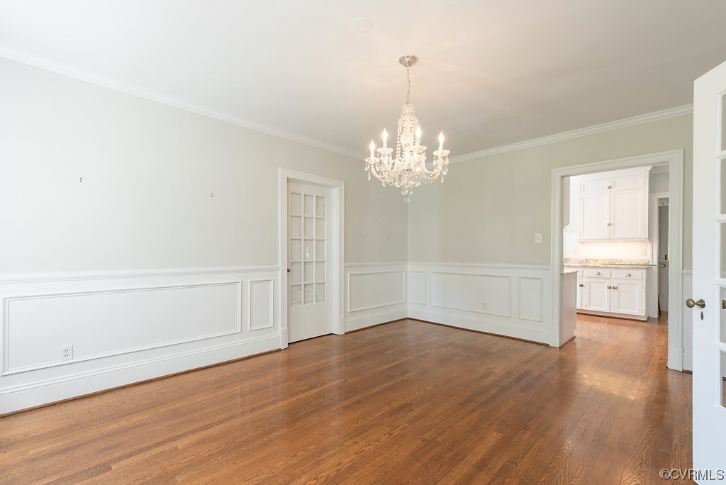 Wood floored empty room featuring crown molding and a chandelier