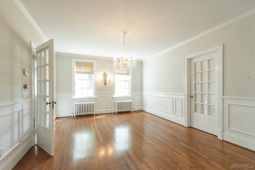 Spare room featuring dark hardwood flooring, an inviting chandelier, crown molding, and radiator heating unit