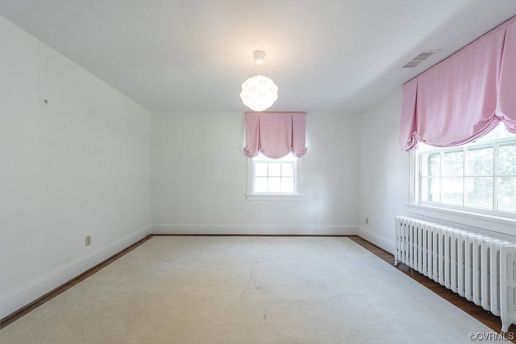 Unfurnished room featuring radiator and a chandelier