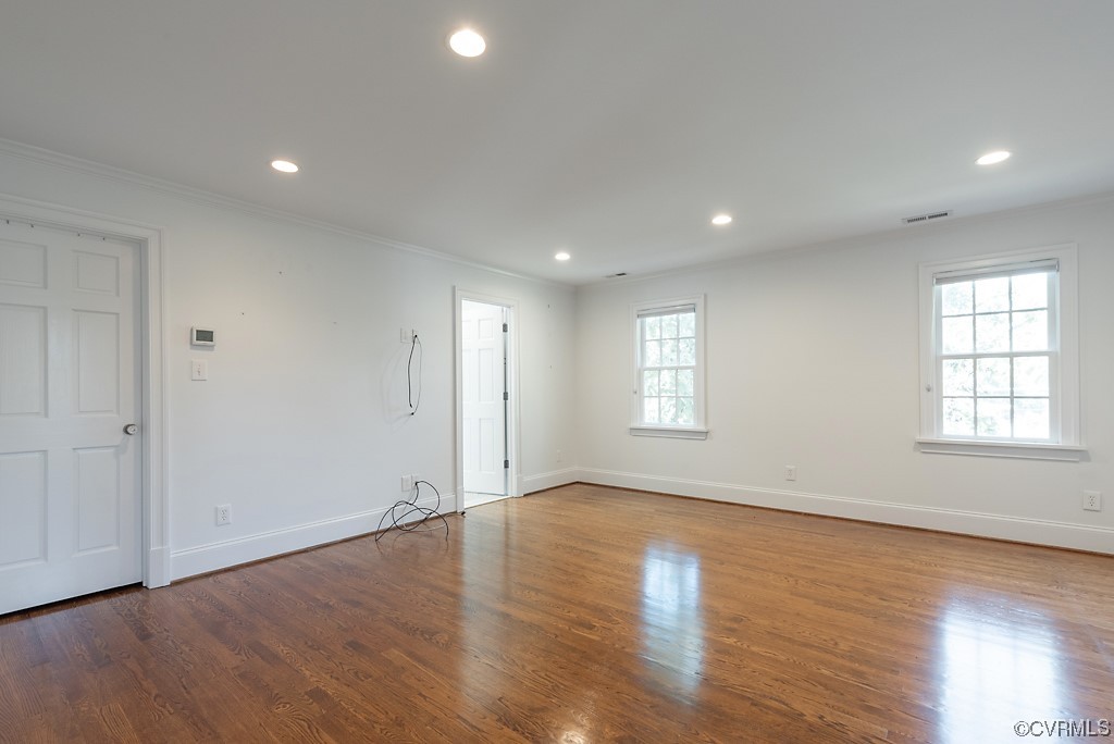 Hardwood floored empty room with crown molding and plenty of natural light