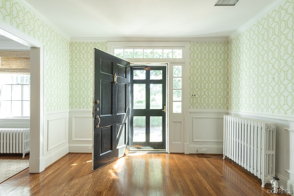 Hardwood floored foyer entrance with radiator heating unit and ornamental molding