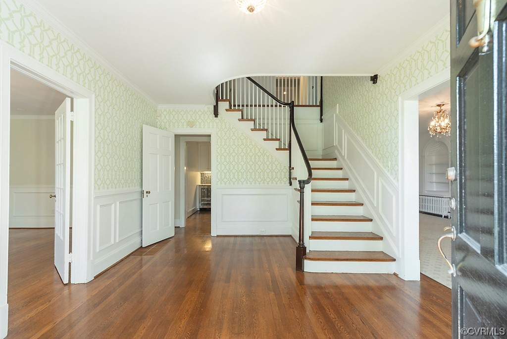 Stairs with dark hardwood flooring, an inviting chandelier, crown molding, and radiator heating unit
