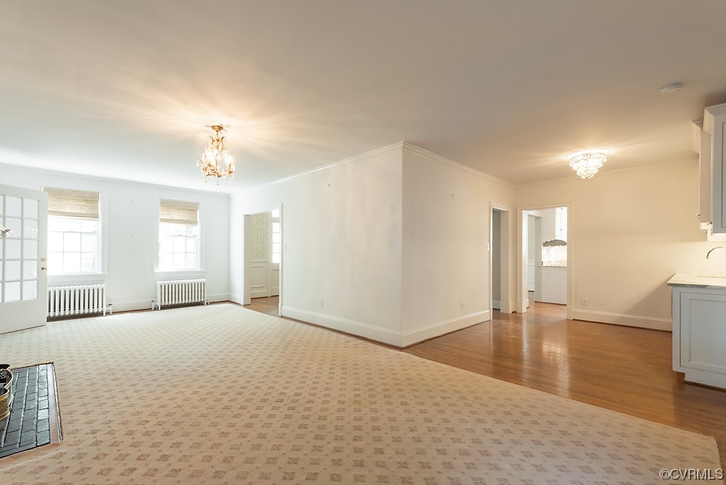 Interior space featuring crown molding, a notable chandelier, radiator heating unit, and light hardwood flooring