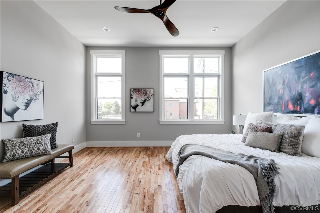 Hardwood floored bedroom featuring multiple windows and ceiling fan
