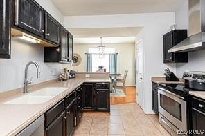 Kitchen featuring sink, light tile floors, hanging light fixtures, wall chimney exhaust hood, and stainless steel appliances