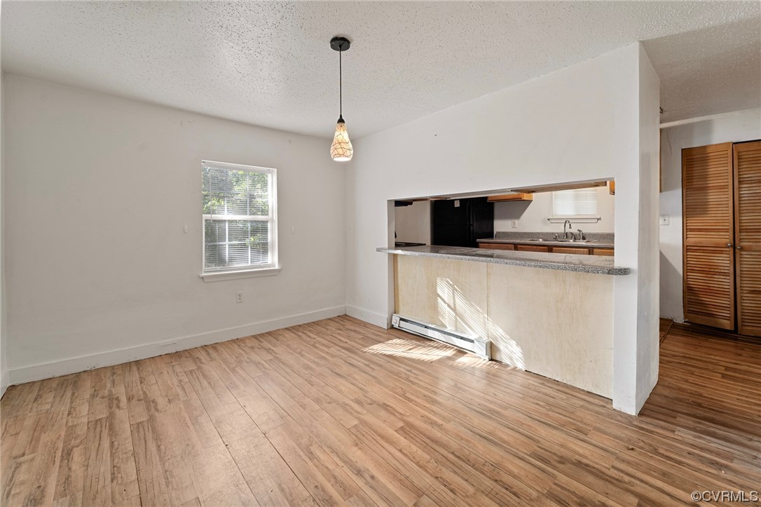 Kitchen with pendant lighting, black fridge, a baseboard heating unit, and light hardwood flooring
