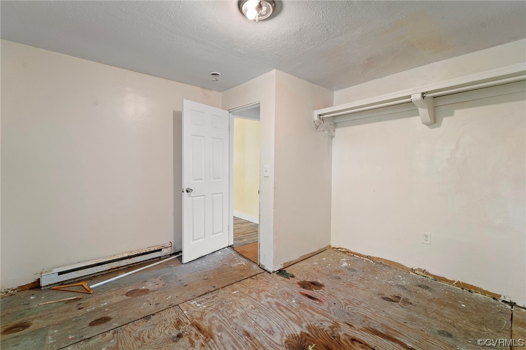 Unfurnished bedroom featuring a textured ceiling and a baseboard heating unit
