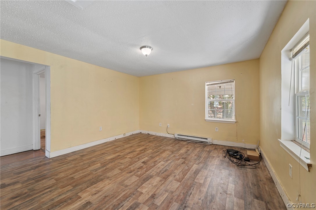 Empty room featuring a textured ceiling, a baseboard heating unit, and dark hardwood floors