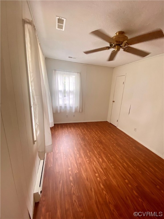 Spare room featuring hardwood / wood-style floors, ceiling fan, a baseboard radiator, and a textured ceiling