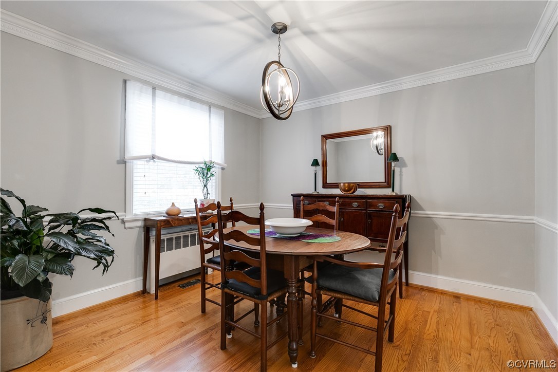 Dining space with crown molding, radiator heating unit, a chandelier, and light hardwood / wood-style flooring