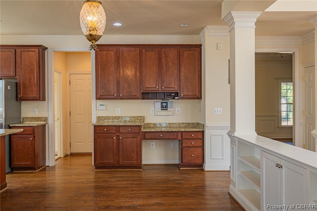 Kitchen featuring light stone counters, dark hardwood / wood-style floors, hanging light fixtures, and ornate columns