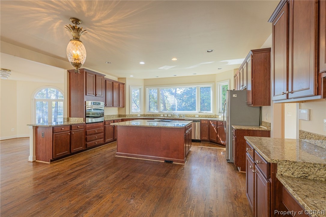 Kitchen with a center island, appliances with stainless steel finishes, dark wood-type flooring, and a healthy amount of sunlight