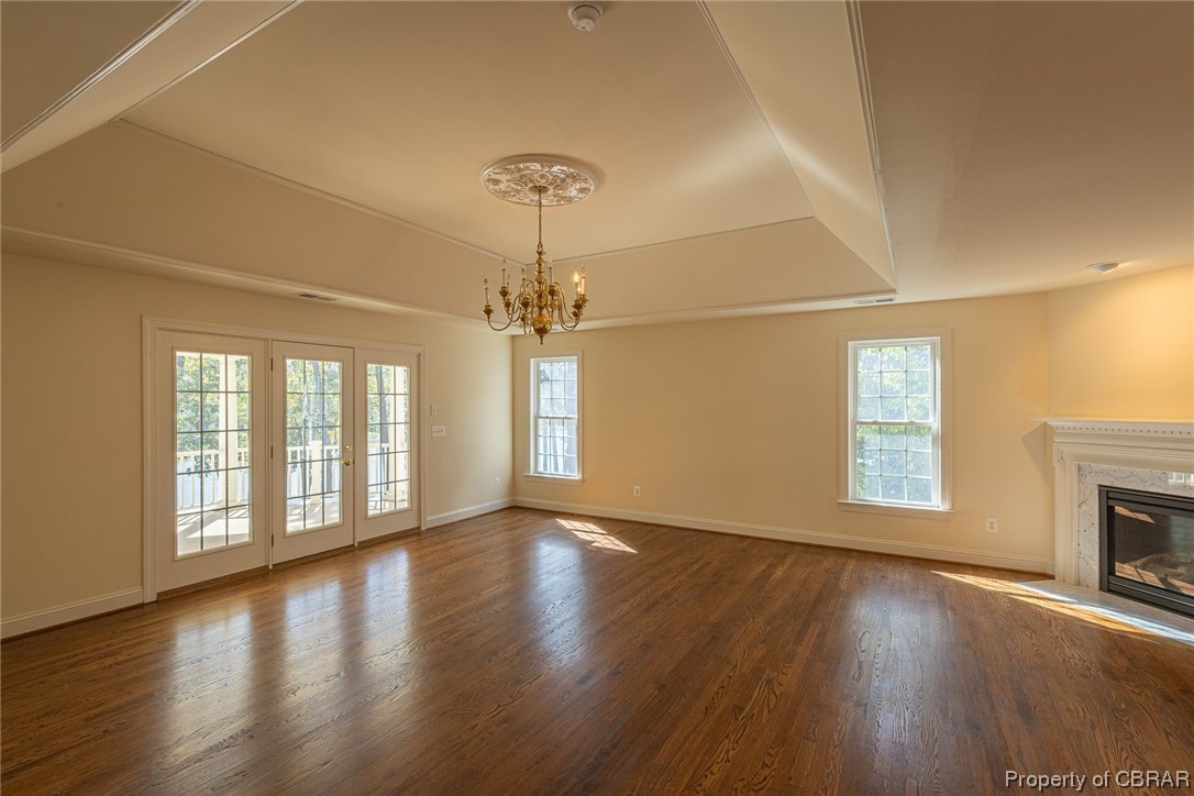 Primary Bedroom with a premium fireplace, a raised ceiling, a chandelier, and dark hardwood / wood-style floors