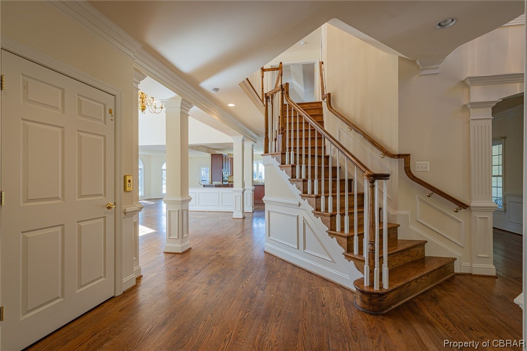 Entrance foyer featuring ornate columns, crown molding, hardwood / wood-style flooring, and a chandelier