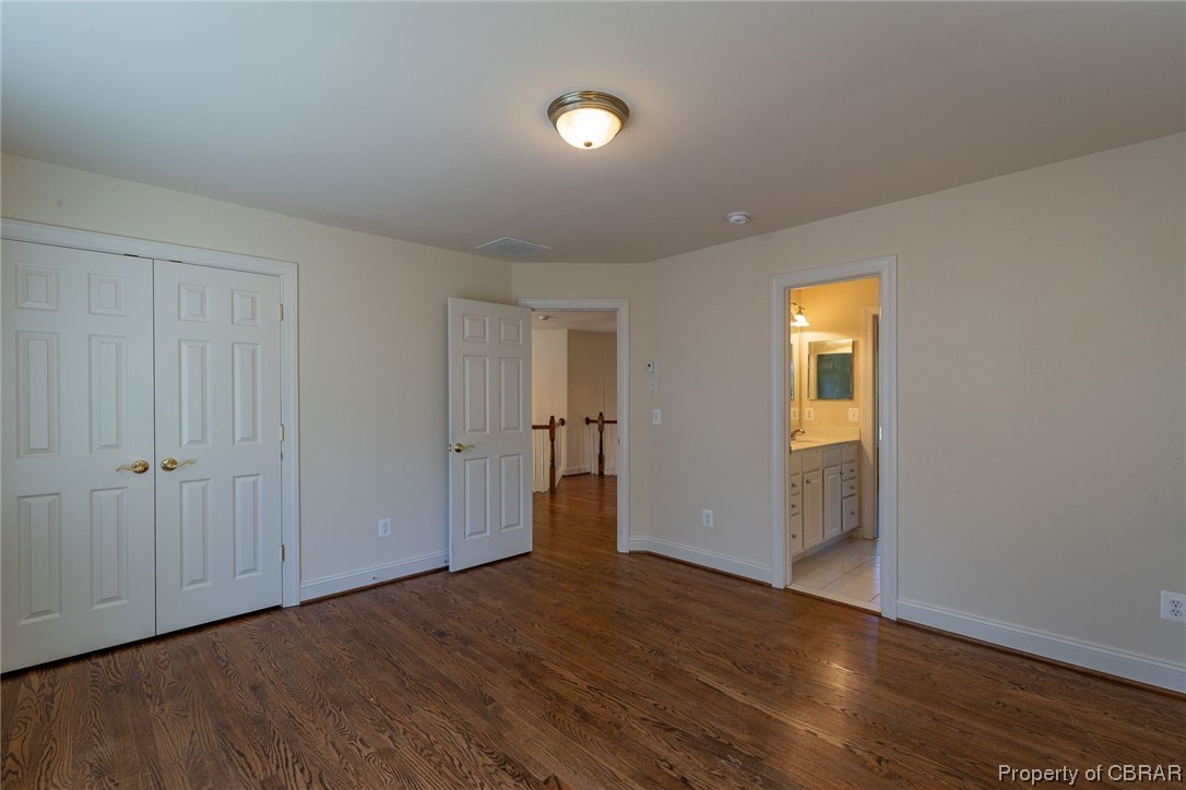 Unfurnished bedroom with hardwood / wood-style flooring, ensuite bathroom, and a closet