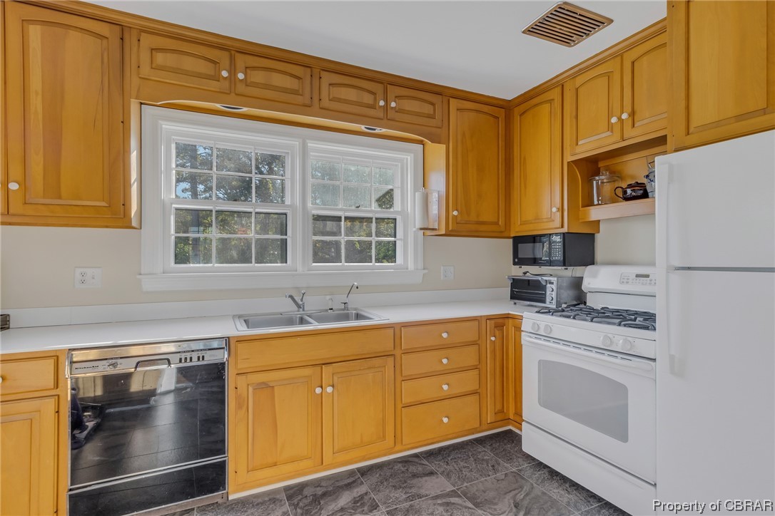 Kitchen with white appliances, dark tile flooring, and sink