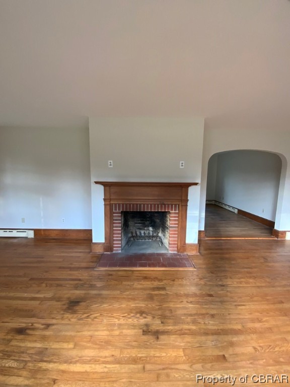 Unfurnished living room featuring dark hardwood / wood-style floors, a brick fireplace, and a baseboard radiator