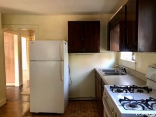Kitchen featuring white fridge, stove, sink, and dark brown cabinets
