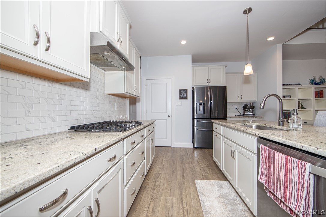 Kitchen with light hardwood / wood-style floors, backsplash, pendant lighting, and sink