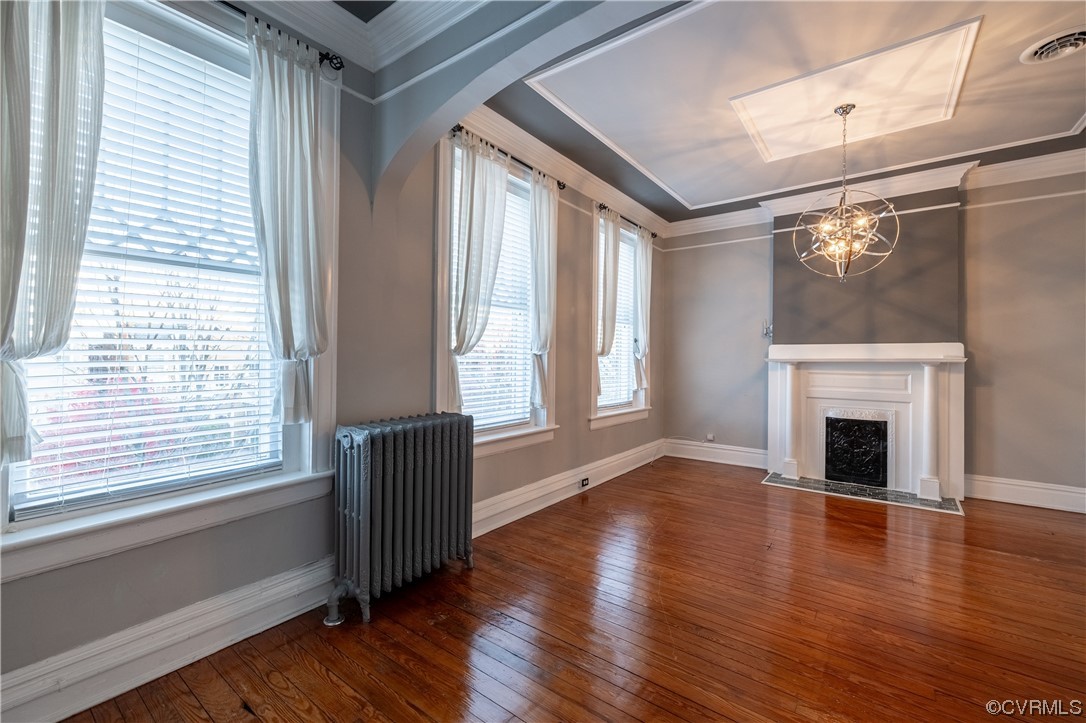 Living room with dark hardwood / wood-style floors, crown molding, radiator, and a notable chandelier