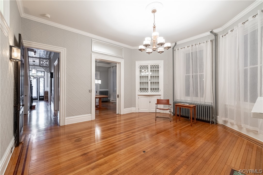 Dining space featuring a wealth of natural light, an inviting chandelier, hardwood / wood-style floors, radiator, and crown molding