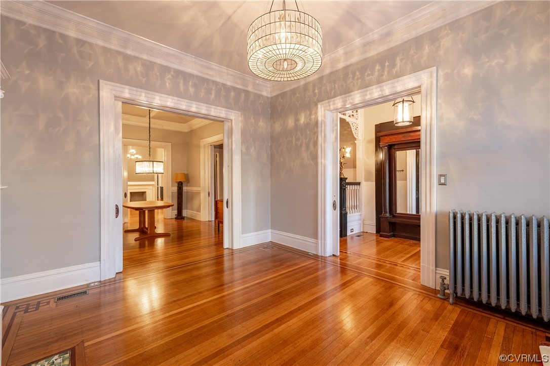 Room with ornamental molding, hardwood / wood-style flooring, a notable chandelier, and radiator heating unit